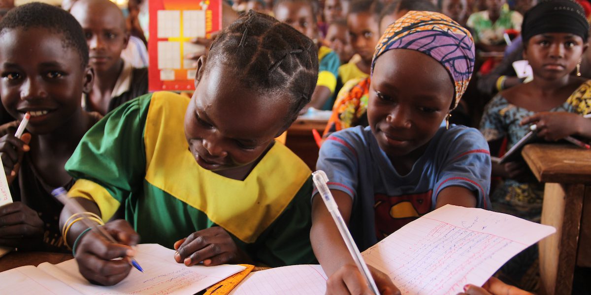A group of students writing on paper while smiling.
