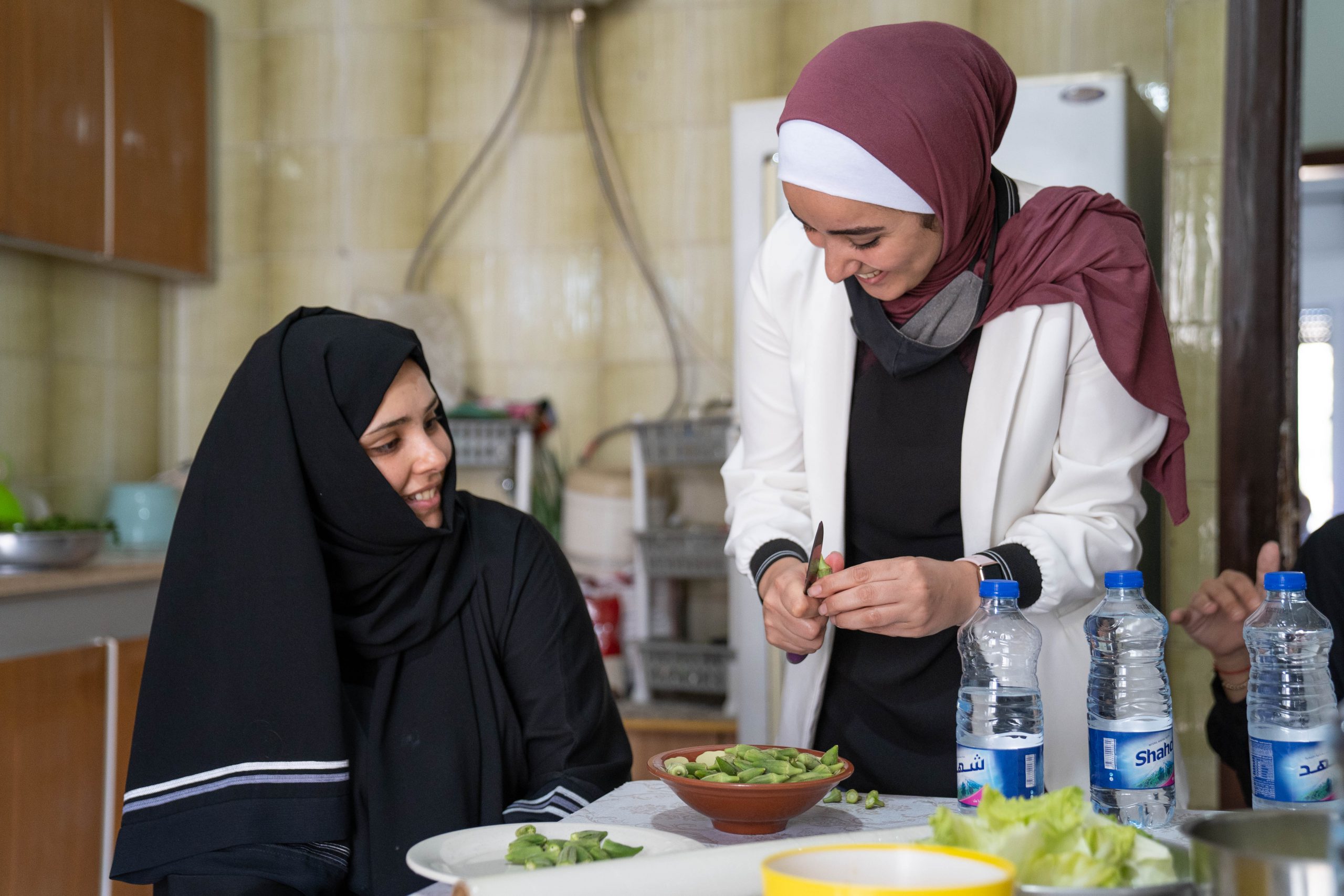 A woman sitting at a table inside a home smiling while another woman is standing over her serving some type of dish.