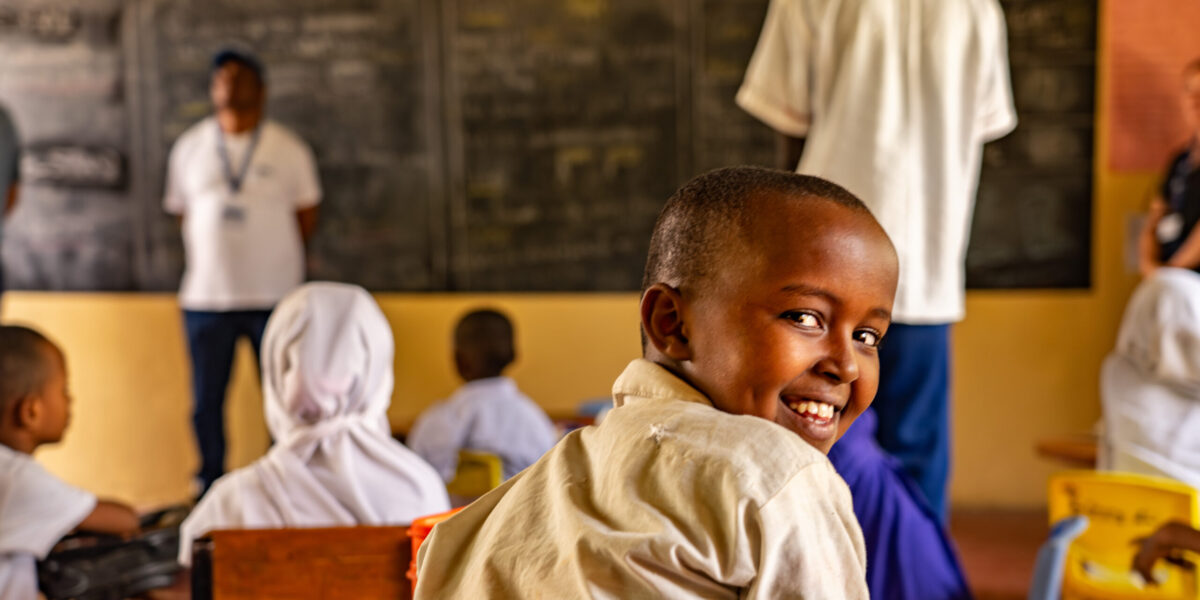 A student looking back at the camera smiling. He is in a classroom with other students