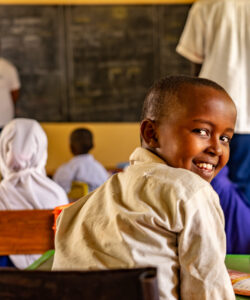 A student looking back at the camera smiling. He is in a classroom with other students