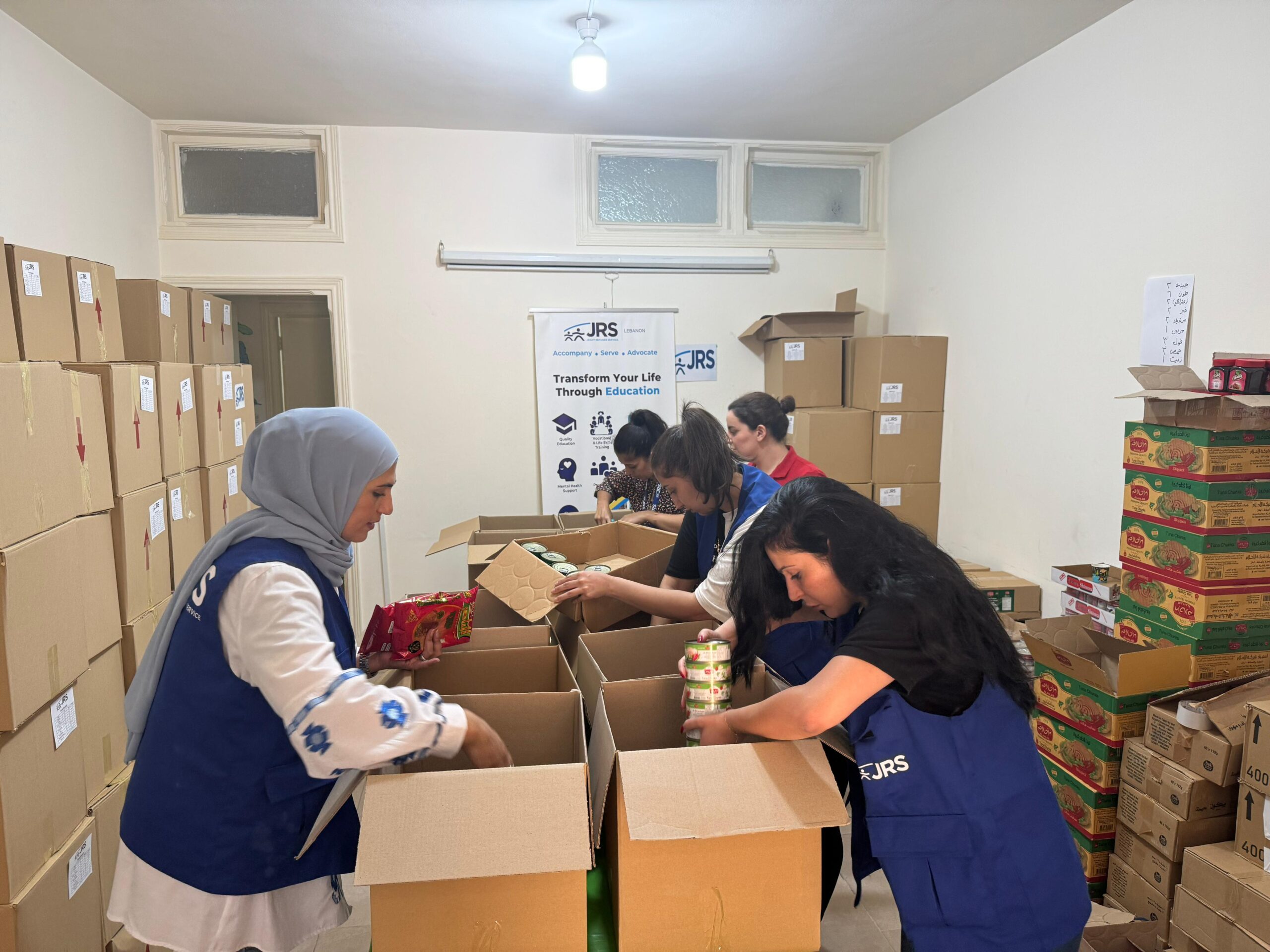JRS staff in Lebanon supporting refugees and other forcibly displaced people with food assistance and other emergency relief amid escalating violence in Lebanon. The staff is packing boxes with various nonperishable food items.