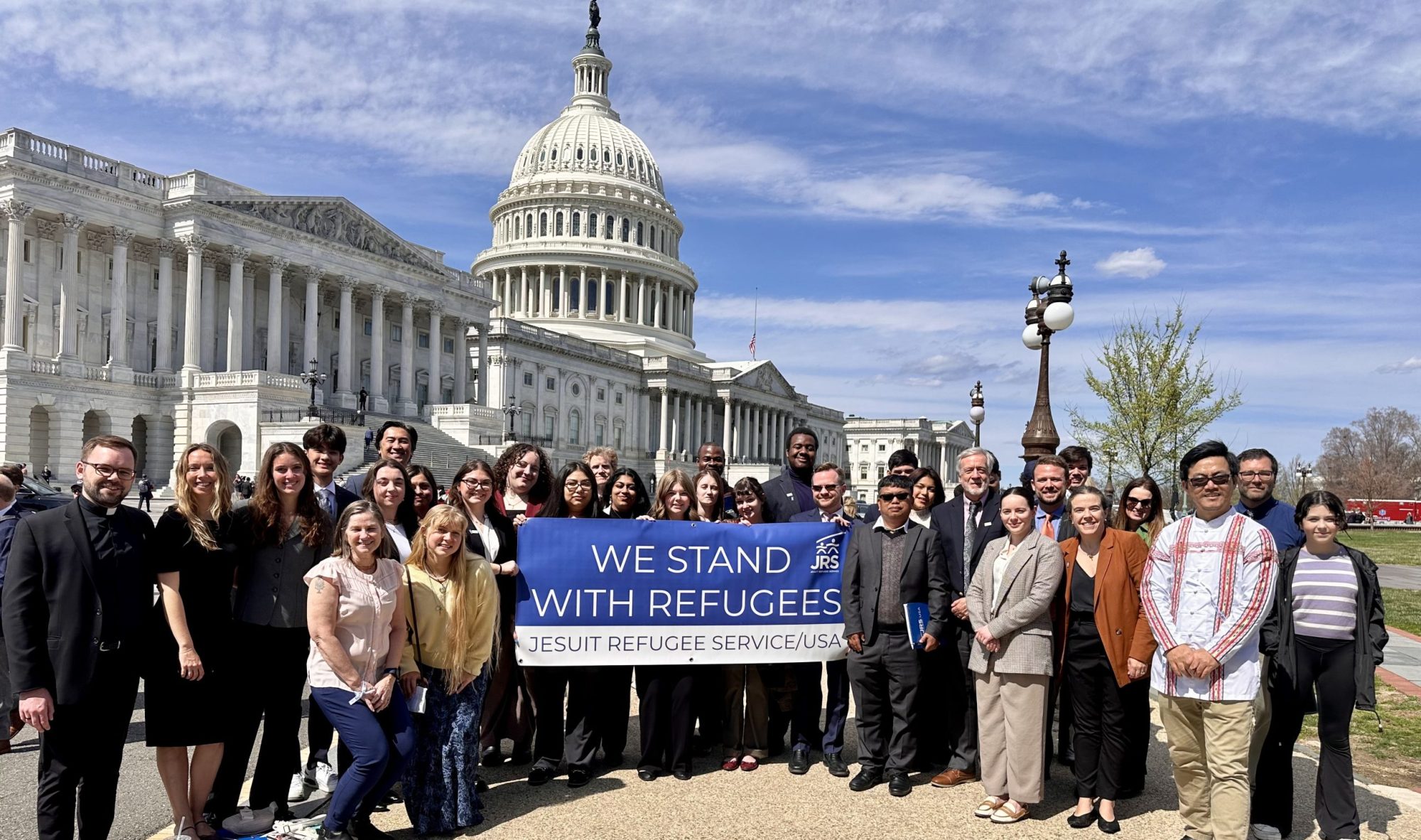 A group of advocates standing in front of the Unted States Capitol building while holding a blue and white banner that says, 